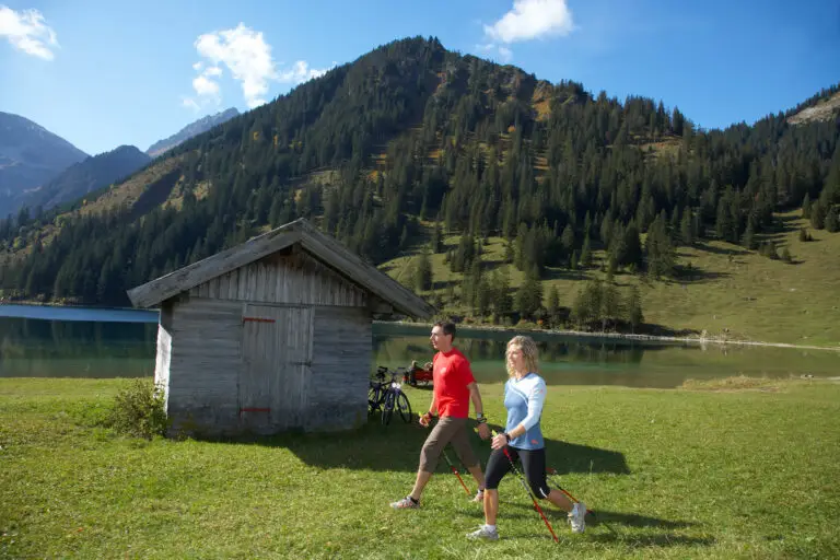 Gruppe von Männer und Frauen beim Nordic Walking in Berglandschaft Kulisse und kleinen See im Vordergrund